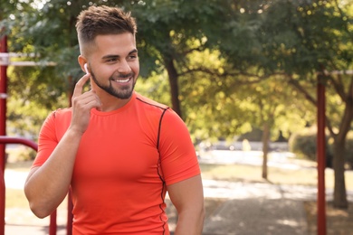 Photo of Young man with wireless headphones listening to music on sports ground. Space for text