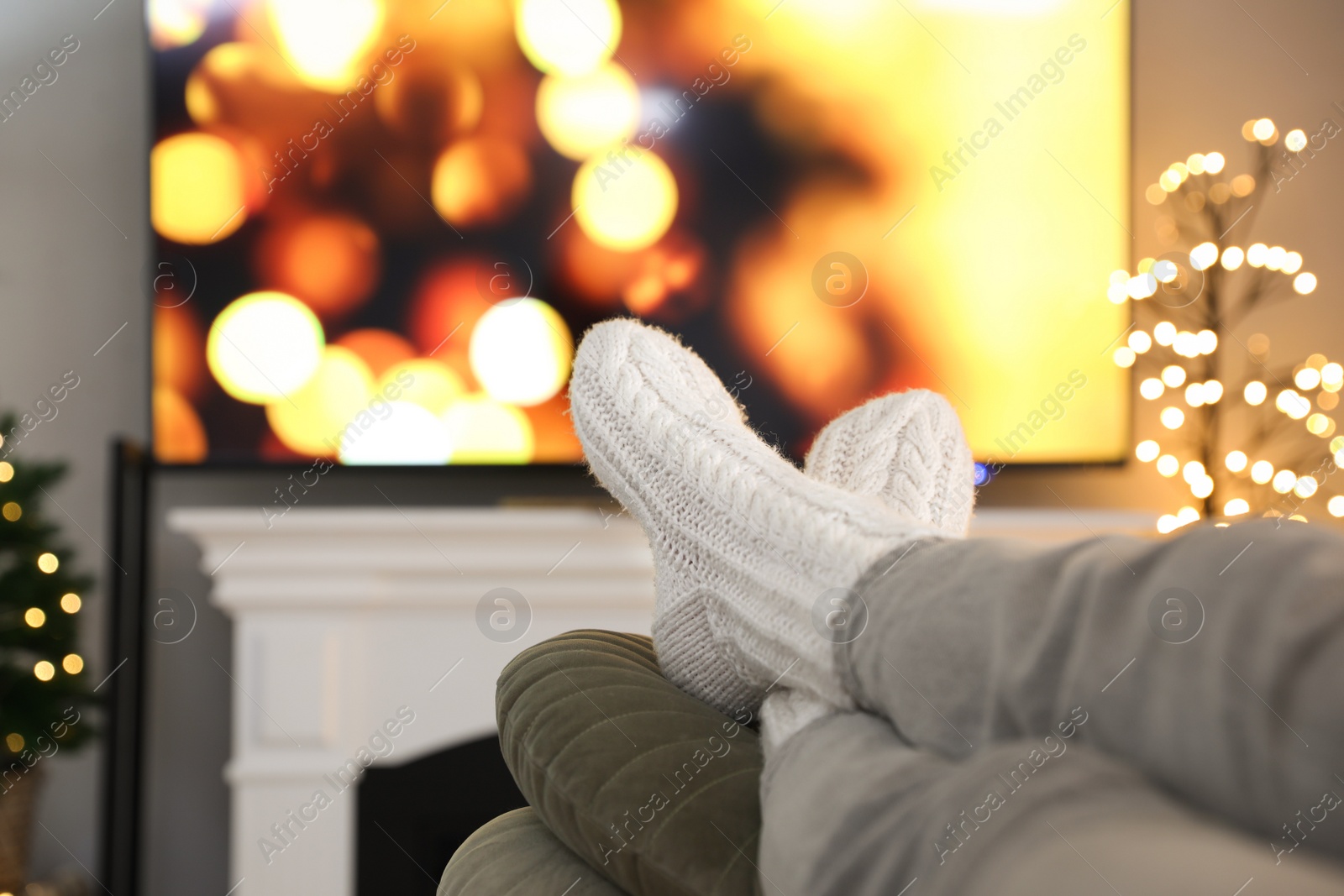 Photo of Woman wearing knitted socks in room decorated for Christmas, closeup