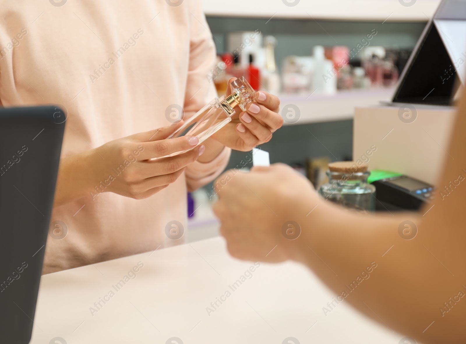 Photo of Young woman helping customer to choose perfume in shop, closeup