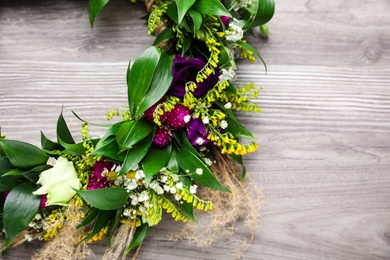 Beautiful wreath made of flowers and leaves on wooden table, top view. Space for text