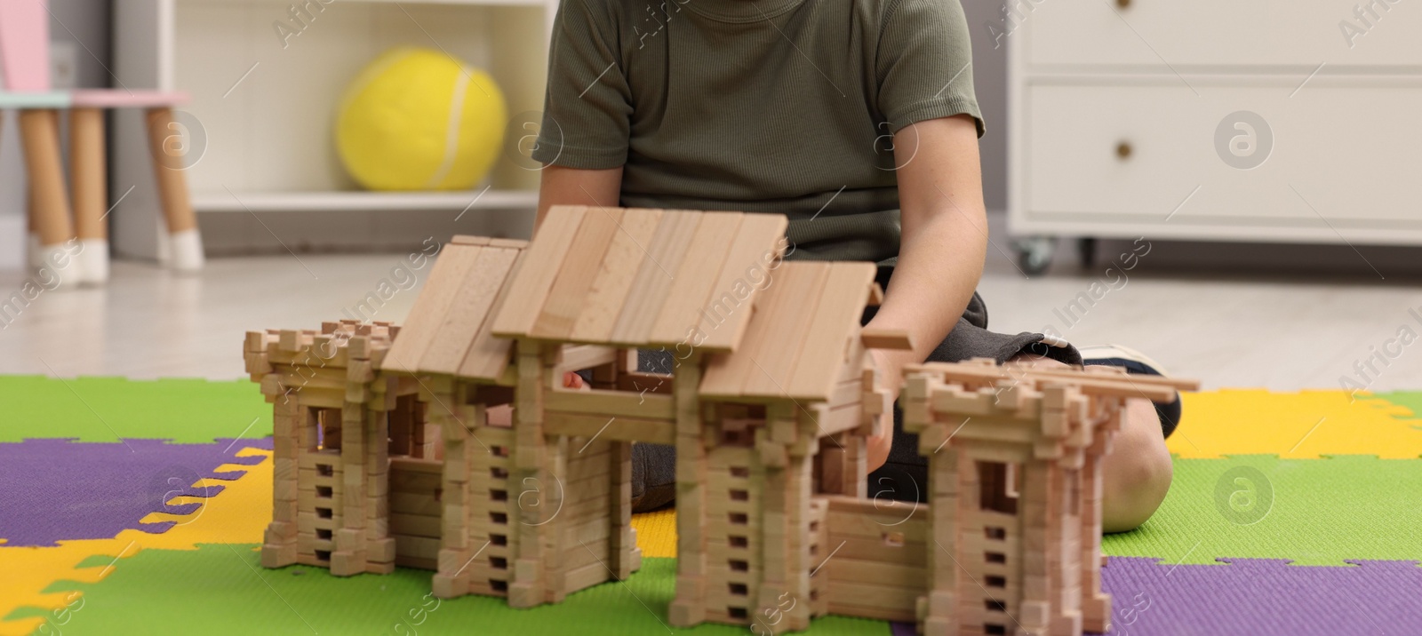 Photo of Little boy playing with wooden entry gate on puzzle mat in room, closeup. Child's toy