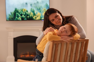 Happy mother hugging sleeping son near fireplace at home