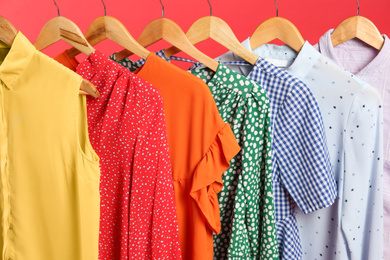 Photo of Bright clothes on hangers against red background, closeup. Rainbow colors