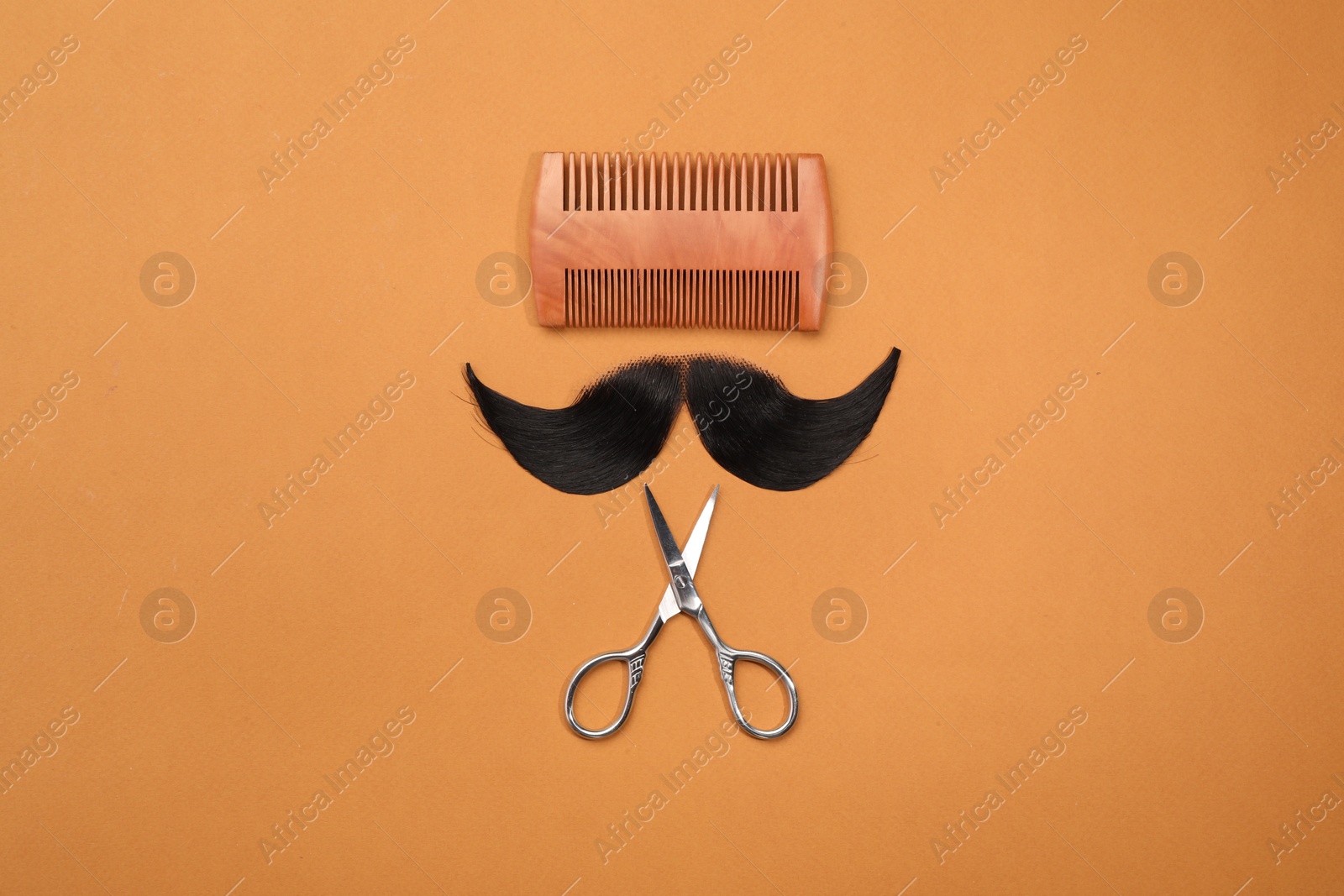 Photo of Artificial moustache, comb and scissors on orange background, top view