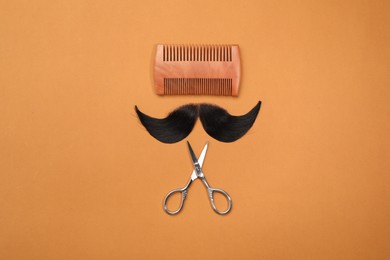 Artificial moustache, comb and scissors on orange background, top view