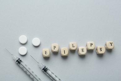 Photo of Word Epilepsy, syringes and pills on light grey background, flat lay. Space for text