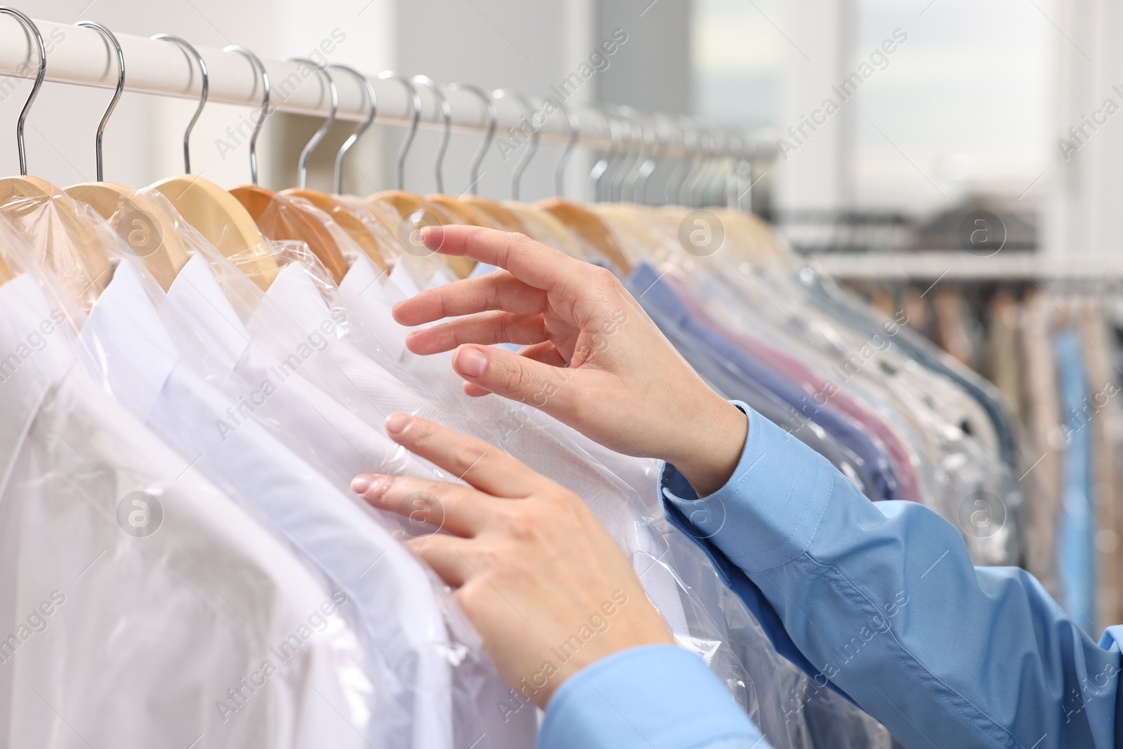 Photo of Dry-cleaning service. Woman taking shirt in plastic bag from rack indoors, closeup