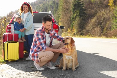 Happy man petting dog, mother and her daughter near car outdoors. Family traveling with pet