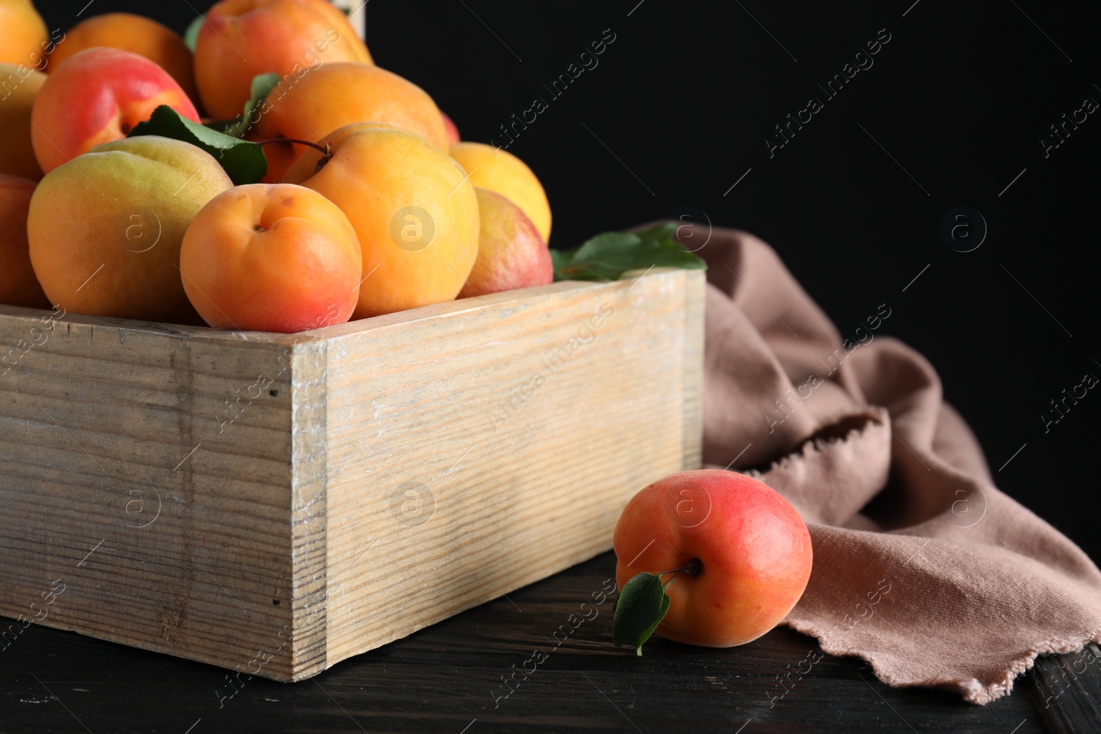 Photo of Many fresh ripe apricots on wooden table against black background