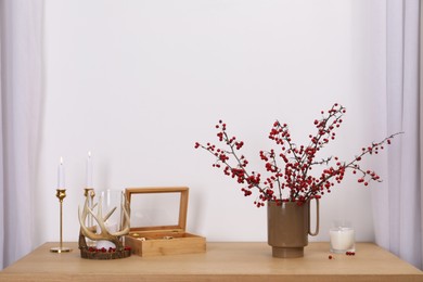 Photo of Hawthorn branches with red berries, box and candles on wooden table indoors