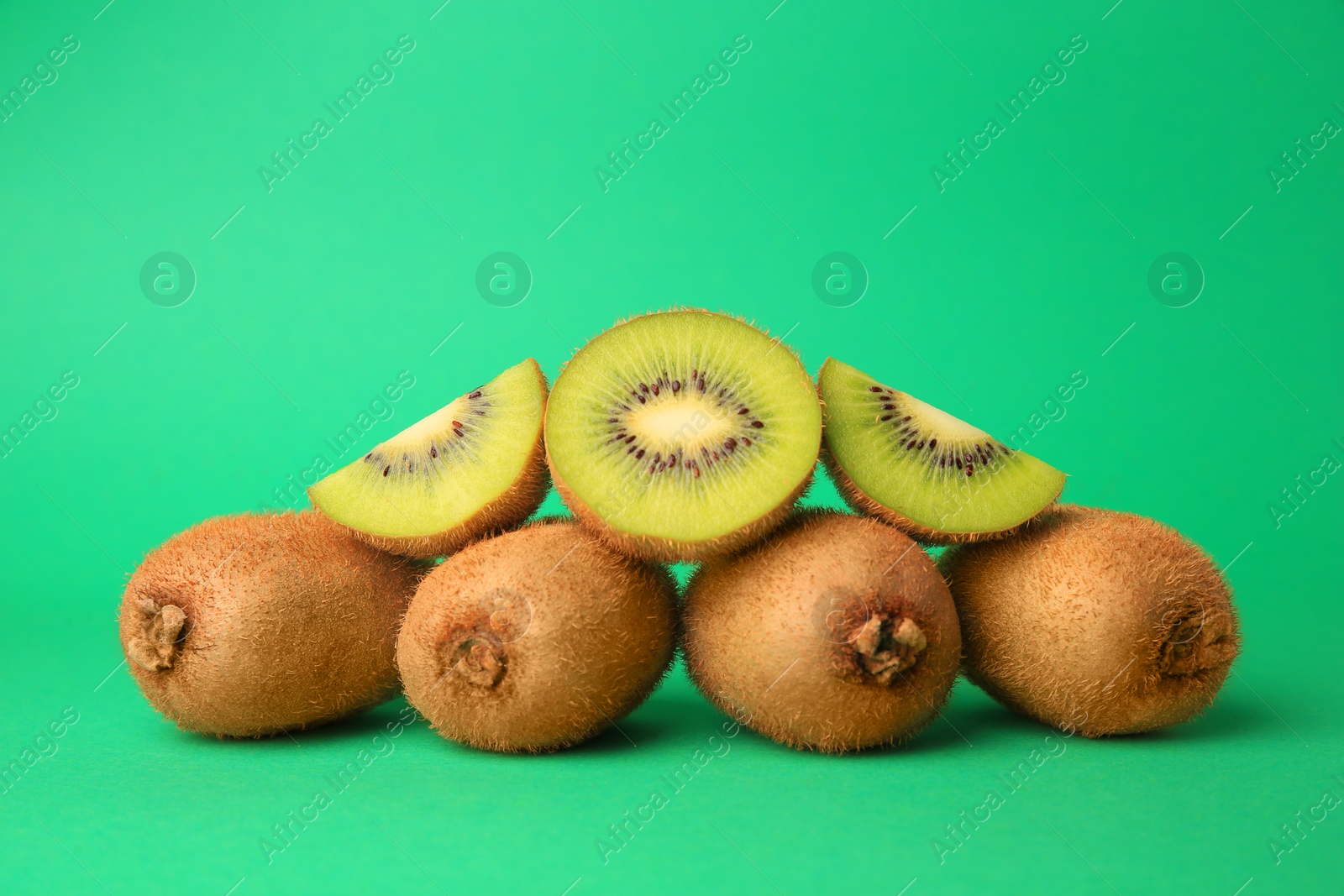 Photo of Heap of whole and cut fresh kiwis on green background