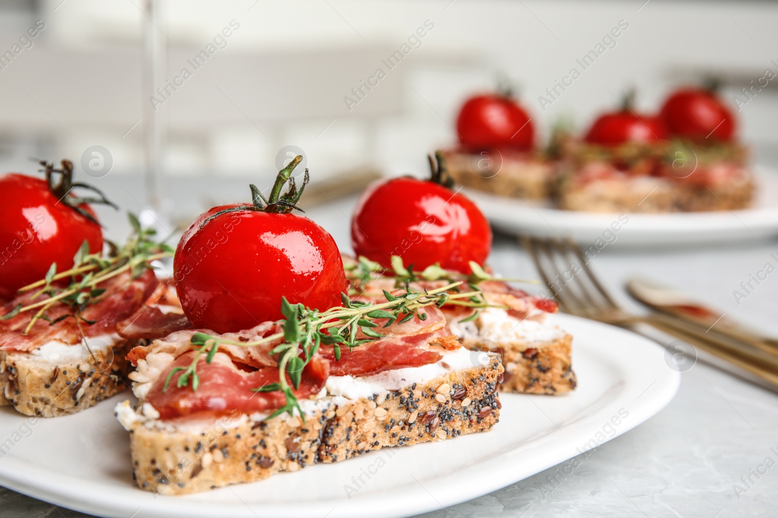 Photo of Plate of delicious bruschettas with prosciutto on grey kitchen table