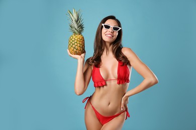 Beautiful woman in stylish bikini with pineapple on blue background