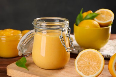 Delicious lemon curd in glass jars, fresh citrus fruits and green leaves on wooden table