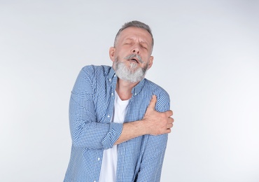 Man suffering from arm pain on light background