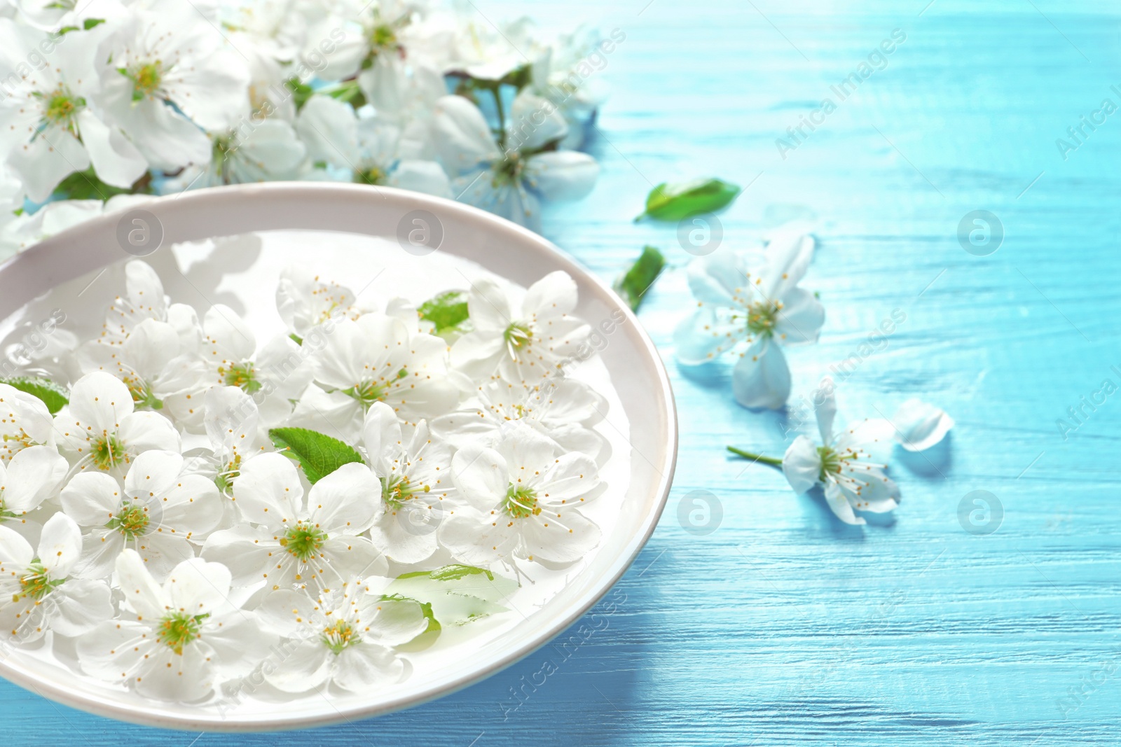 Photo of Bowl with water and blossoming flowers on wooden background