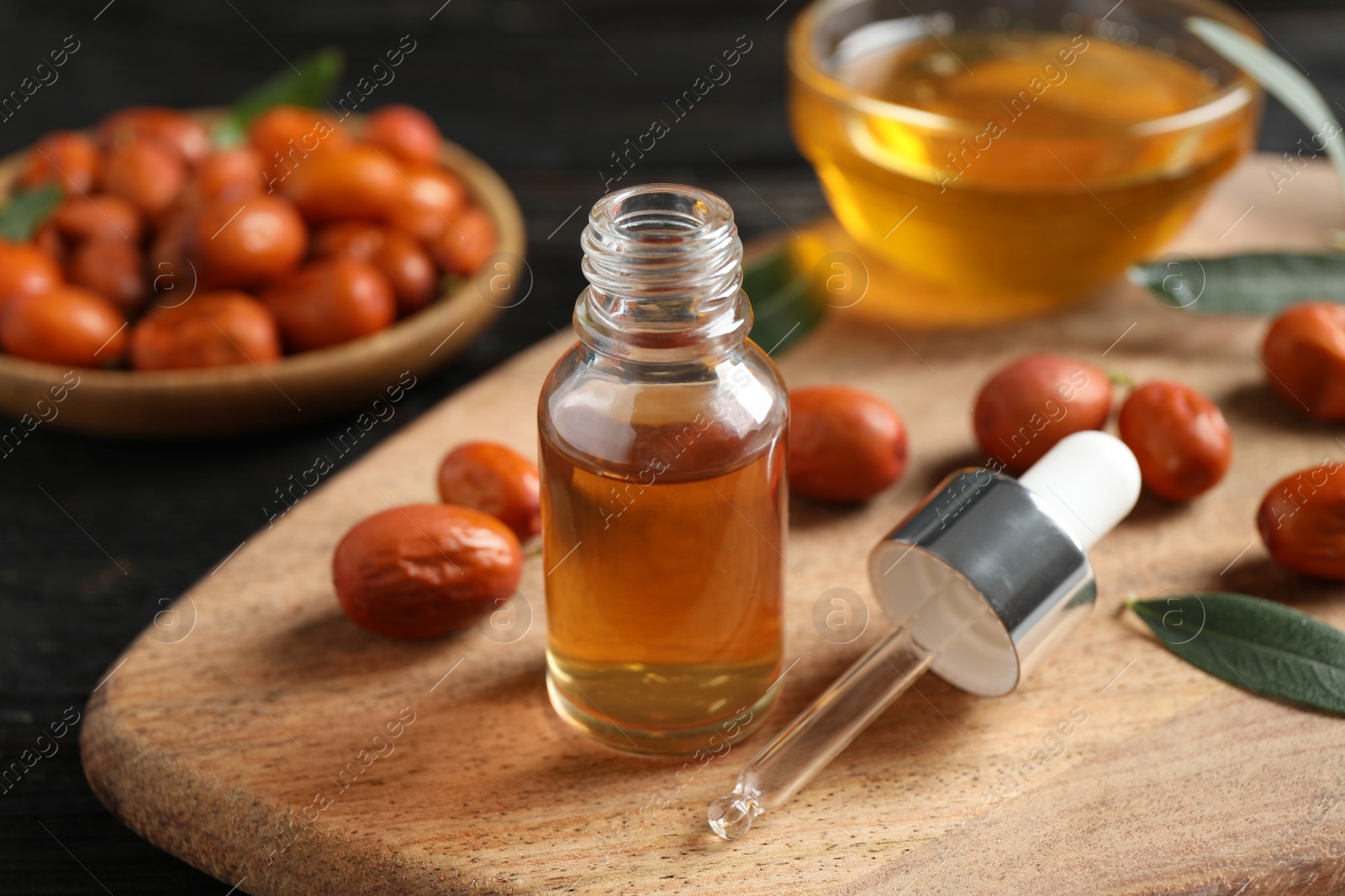Photo of Glass bottle with jojoba oil and seeds on black wooden table