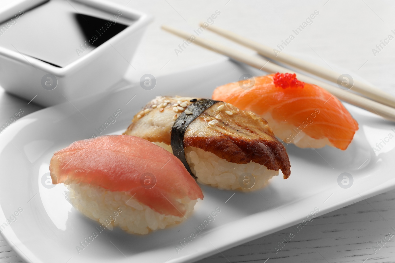 Photo of Plate with delicious nigiri sushi and soy sauce on white wooden table, closeup