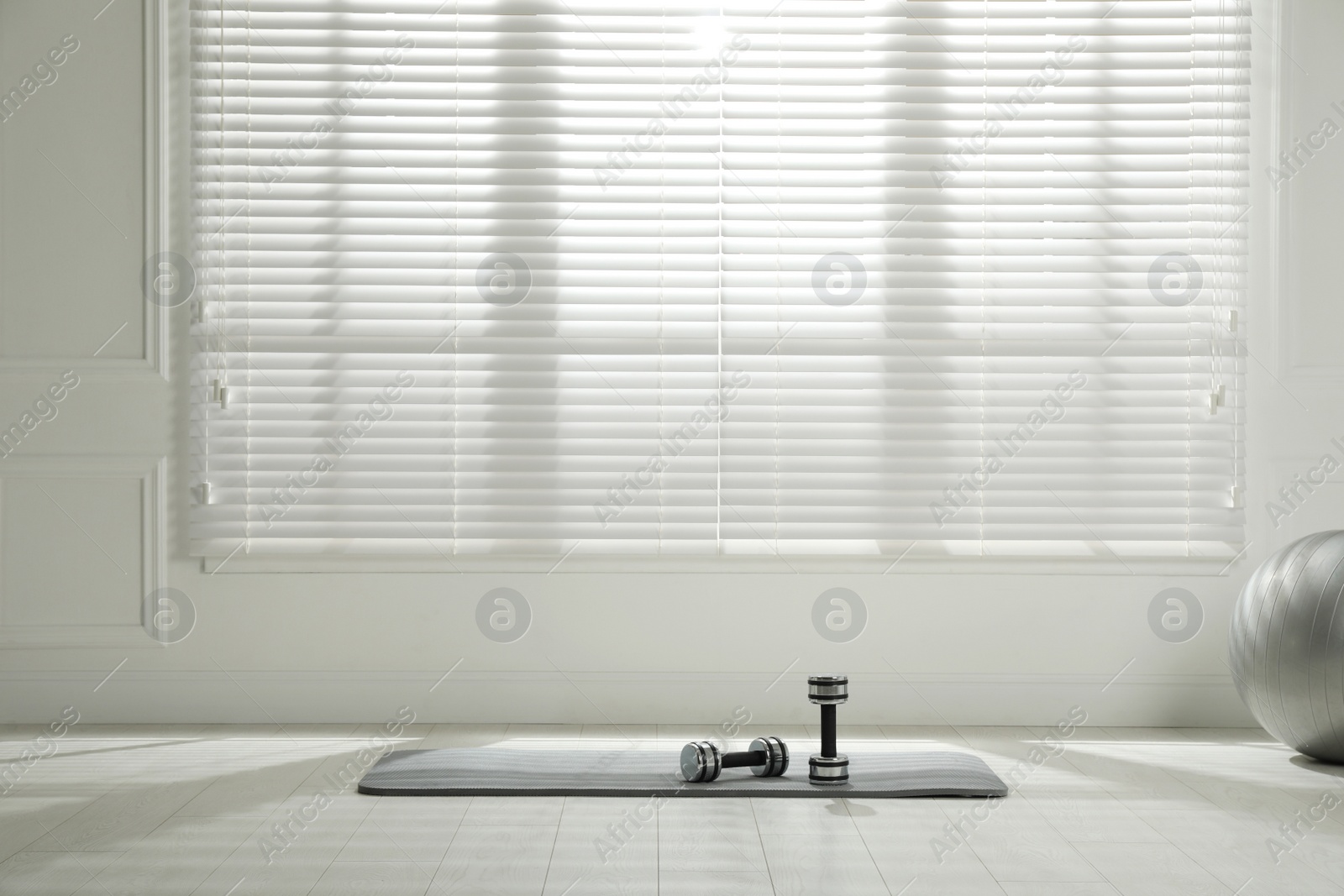 Photo of Mat, dumbbells and fitness ball near window in room