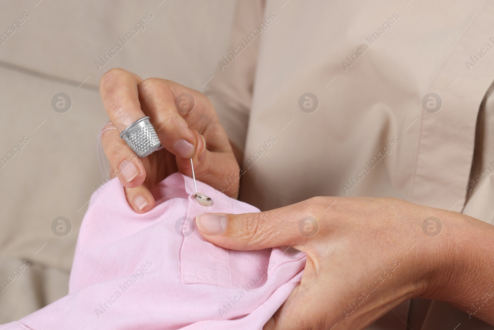 Photo of Woman sewing button with thimble and needle, closeup