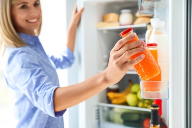 Photo of Woman taking bottle with juice out of refrigerator in kitchen