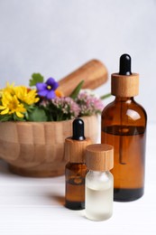 Glass bottles of aromatic essential oil, mortar with different wildflowers on white wooden table