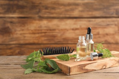 Photo of Stinging nettle extract and brush on wooden background, space for text. Natural hair care