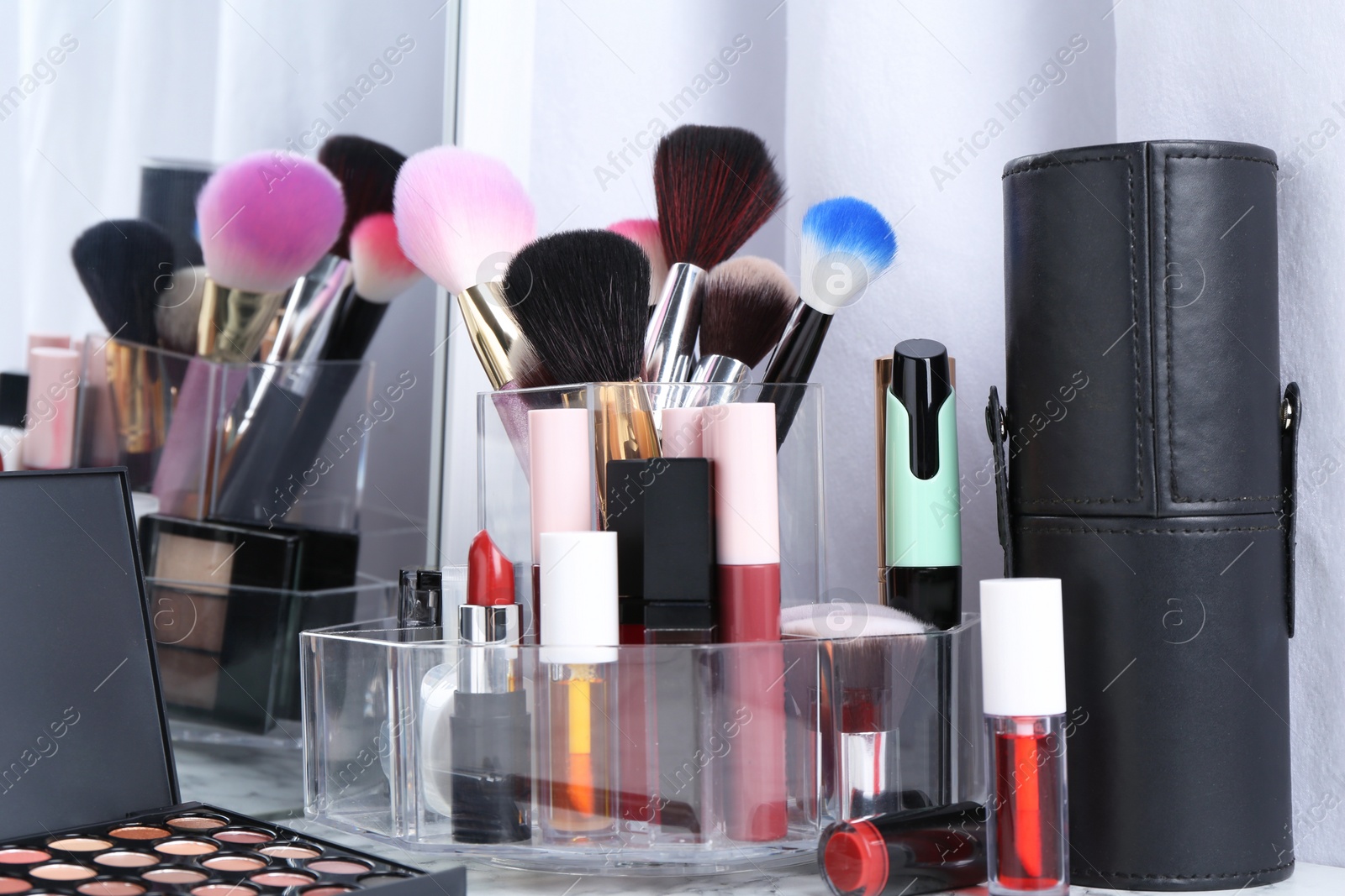 Photo of Bright lip glosses among different cosmetic products on white dressing table