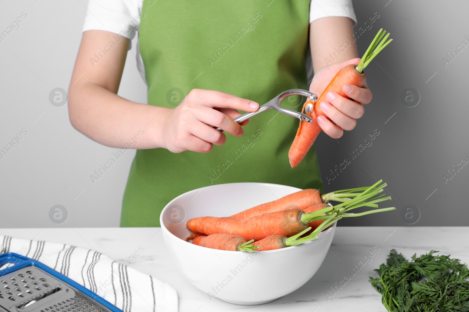 Photo of Woman peeling fresh carrot at white table indoors