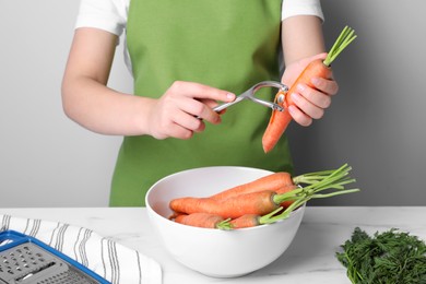 Photo of Woman peeling fresh carrot at white table indoors