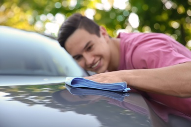 Young man washing car hood with rag outdoors