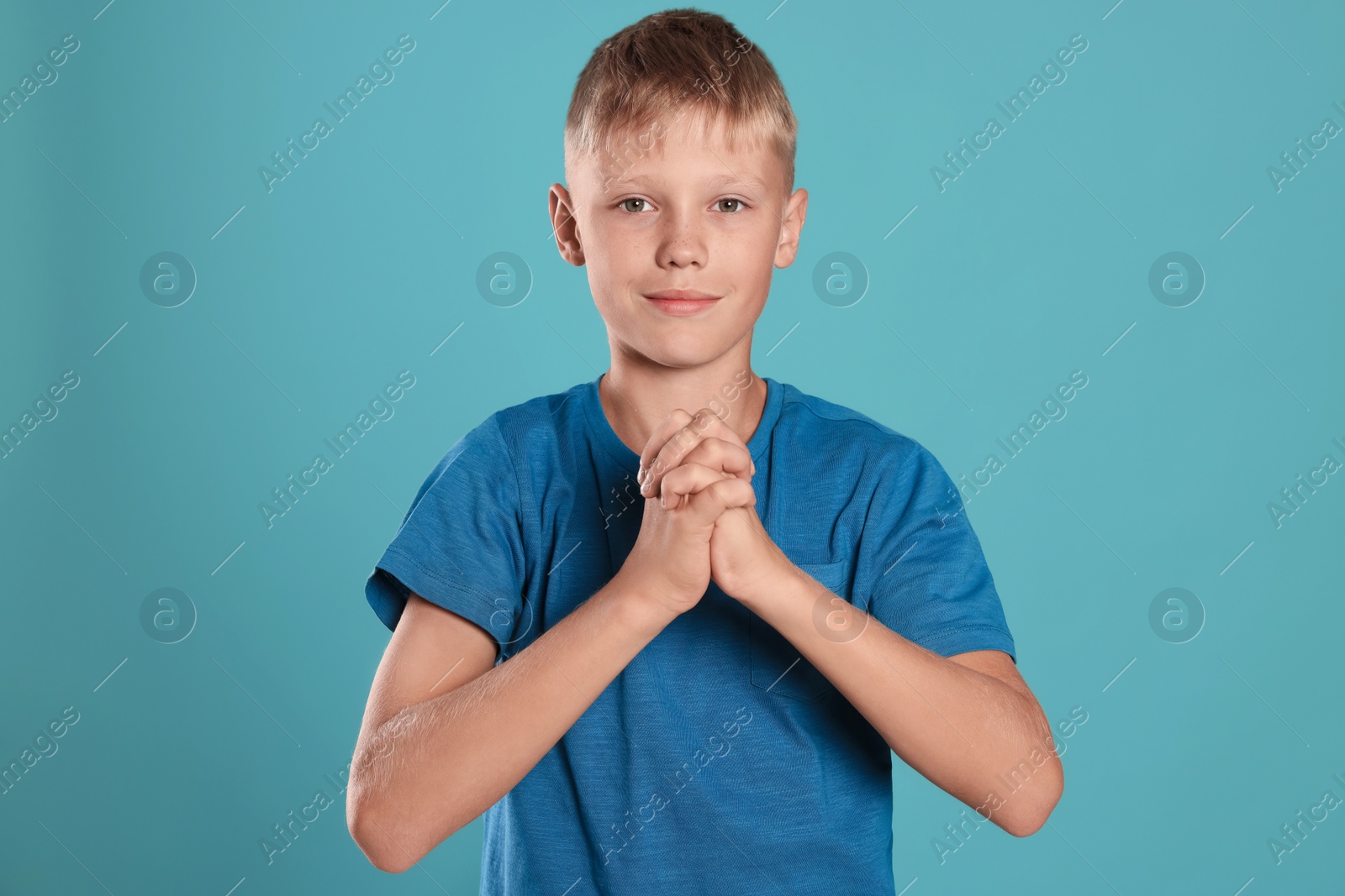 Photo of Boy with clasped hands praying on turquoise background