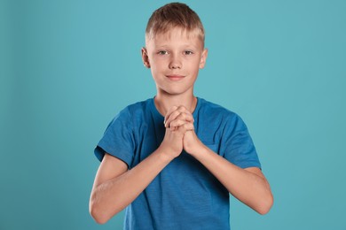 Photo of Boy with clasped hands praying on turquoise background