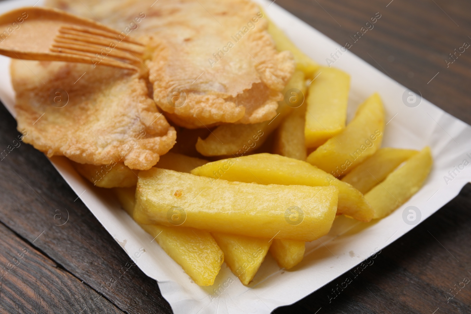 Photo of Delicious fish and chips served on wooden table, closeup