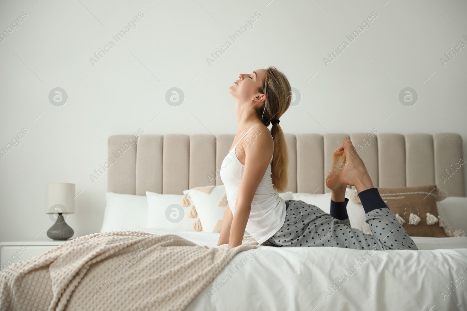 Photo of Young woman doing gymnastics on bed at home. Morning fitness