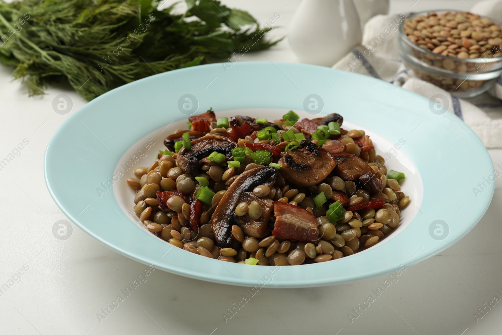 Photo of Delicious lentils with mushrooms, bacon and green onion on white table, closeup