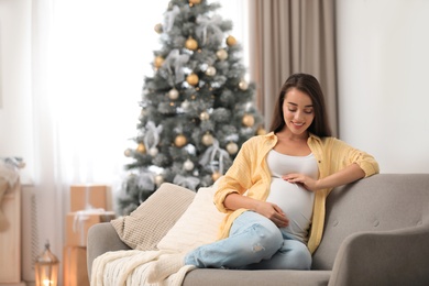 Happy pregnant woman on sofa in living room decorated for Christmas. Expecting baby