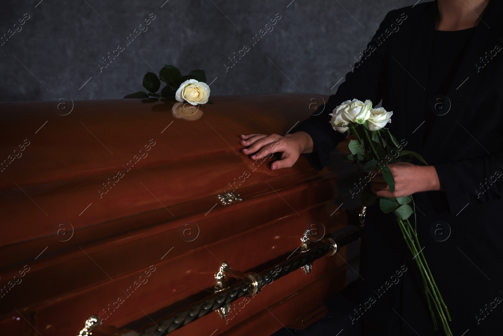 Photo of Young woman with white roses near casket in funeral home, closeup