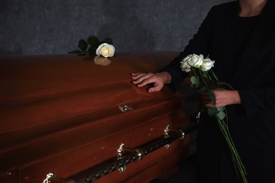 Photo of Young woman with white roses near casket in funeral home, closeup