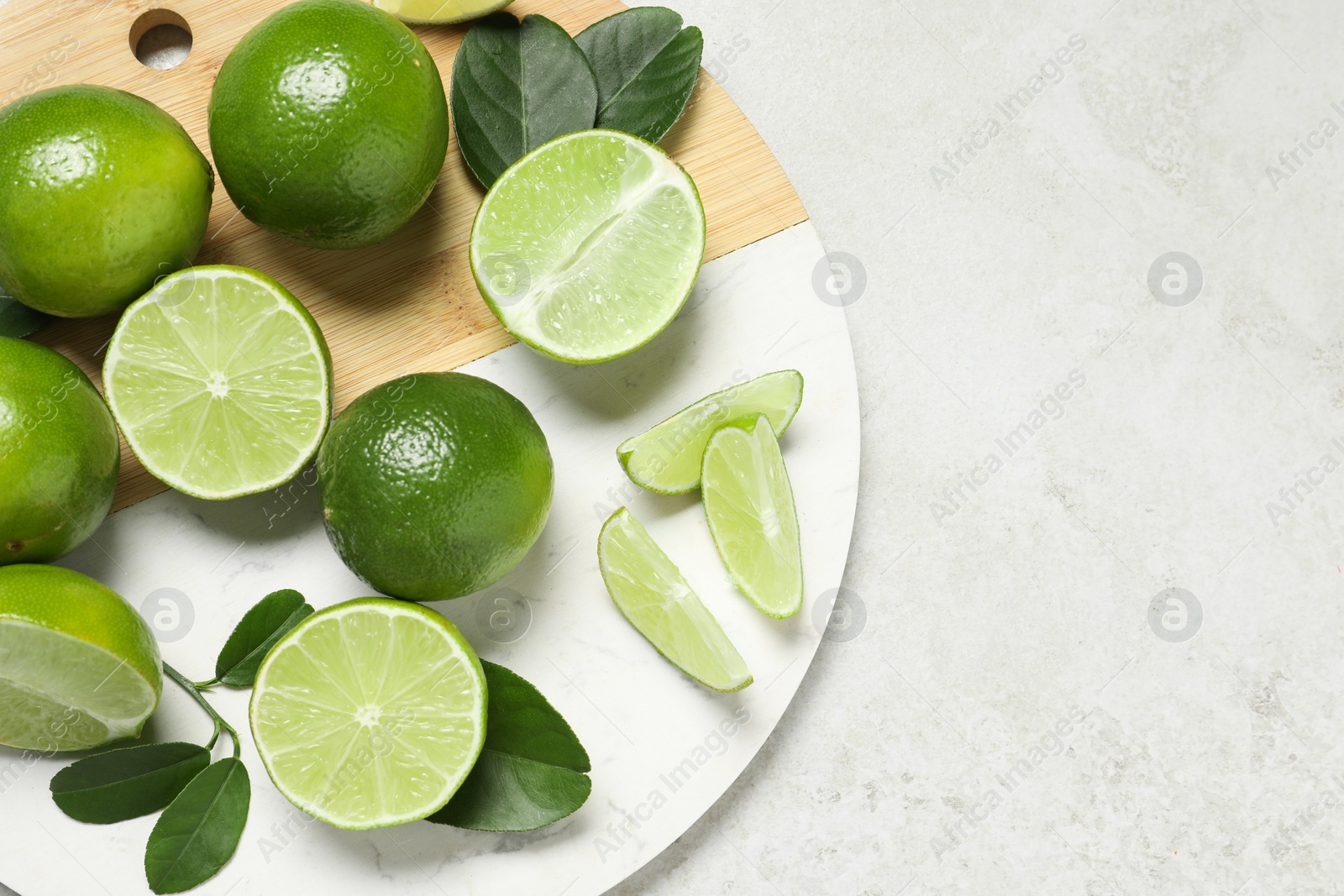 Photo of Fresh ripe limes and leaves on light table, top view. Space for text