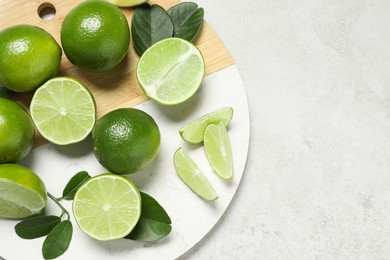 Fresh ripe limes and leaves on light table, top view. Space for text