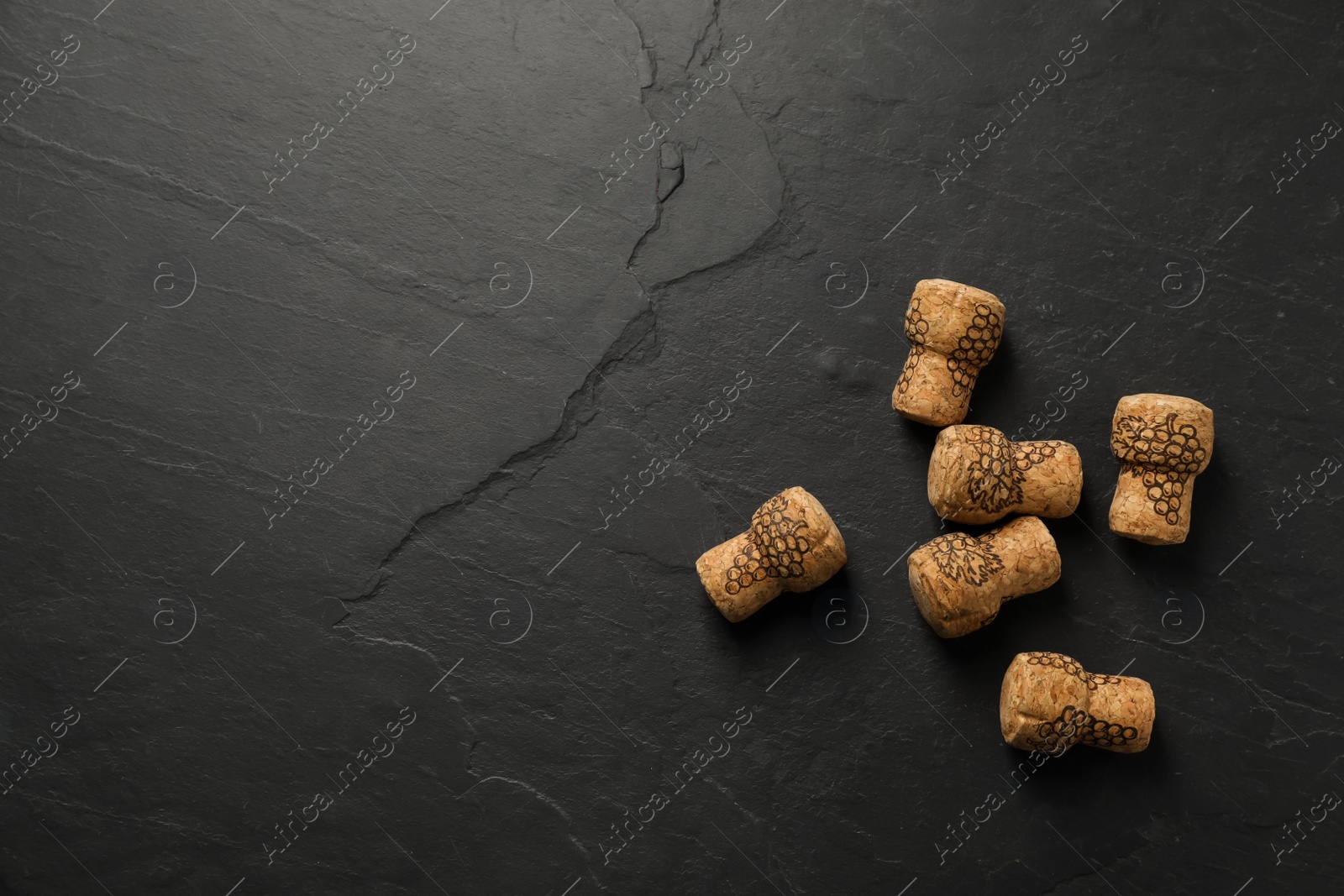 Photo of Sparkling wine corks with grape images on black table, flat lay. Space for text