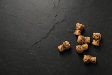 Photo of Sparkling wine corks with grape images on black table, flat lay. Space for text