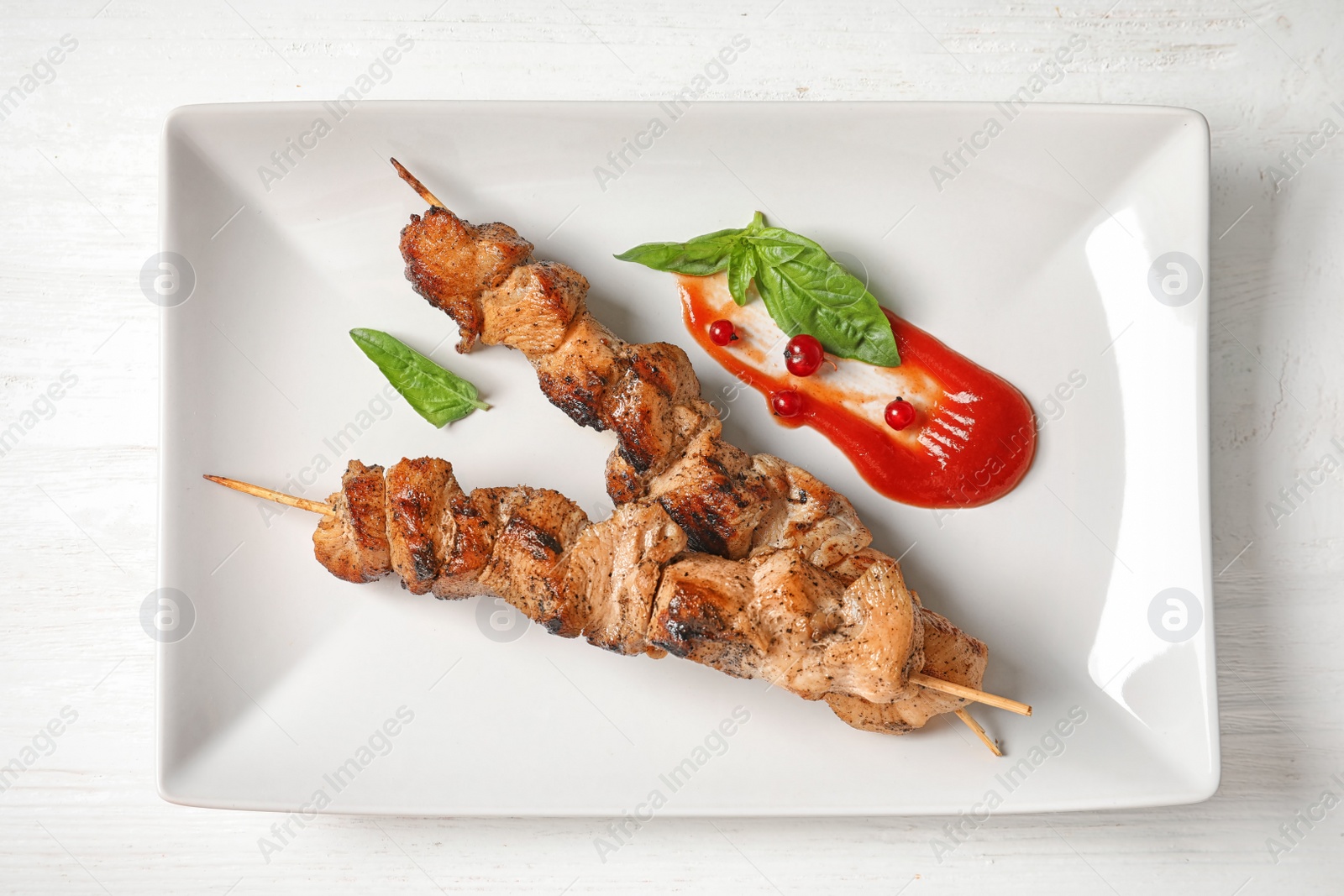 Photo of Plate with juicy shish kebab and sauce on table, top view