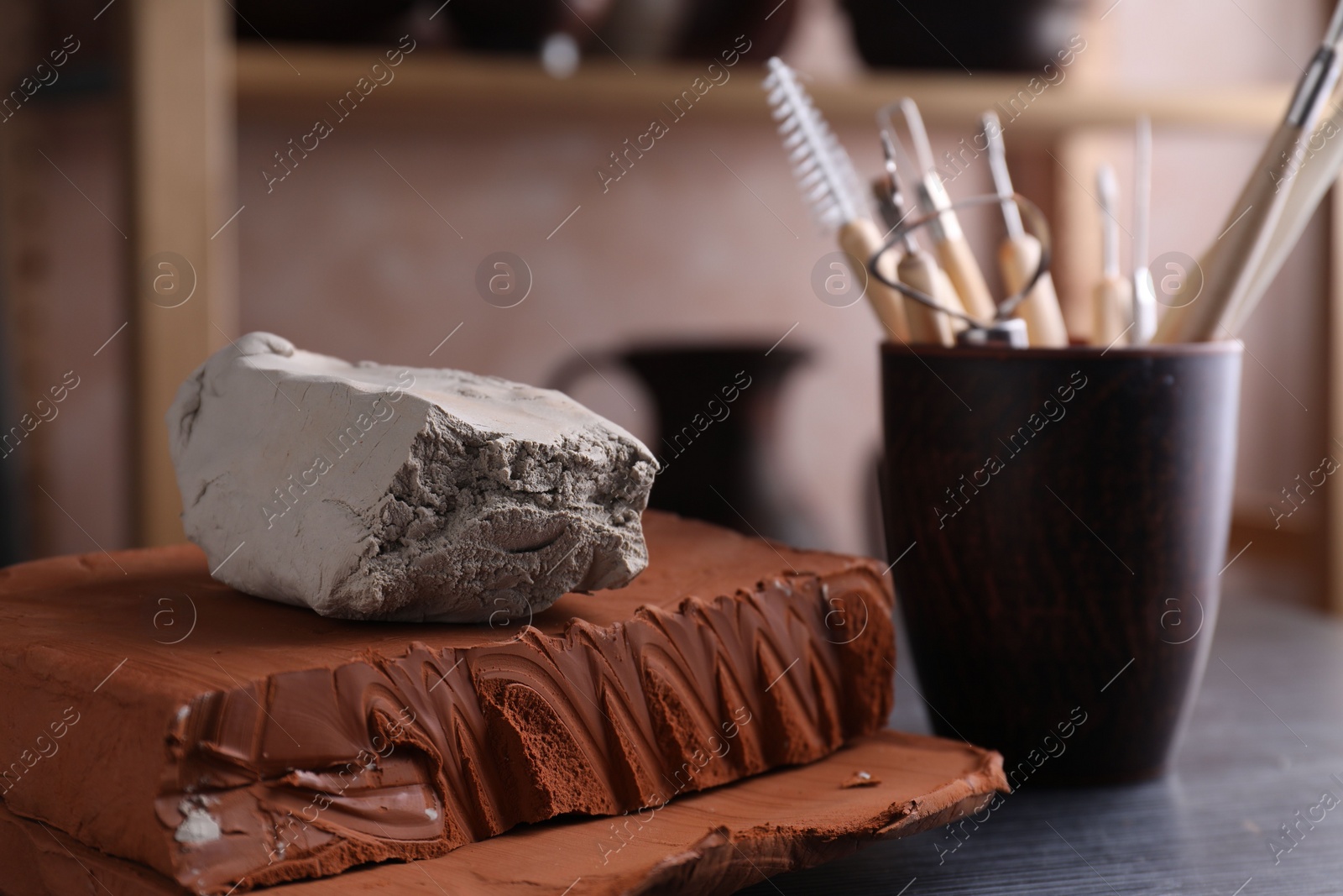 Photo of Clay and set of modeling tools on dark gray table in workshop, closeup