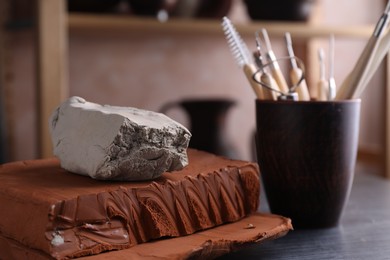 Photo of Clay and set of modeling tools on dark gray table in workshop, closeup