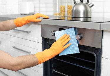 Photo of Young man cleaning oven with rag in kitchen, closeup