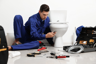 Professional plumber working with toilet bowl in bathroom