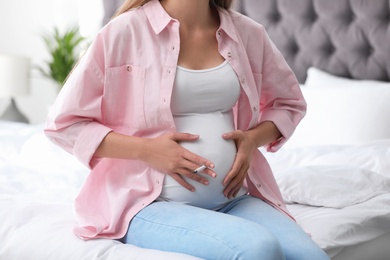 Young pregnant woman smoking cigarette in bedroom, closeup. Harm to unborn baby