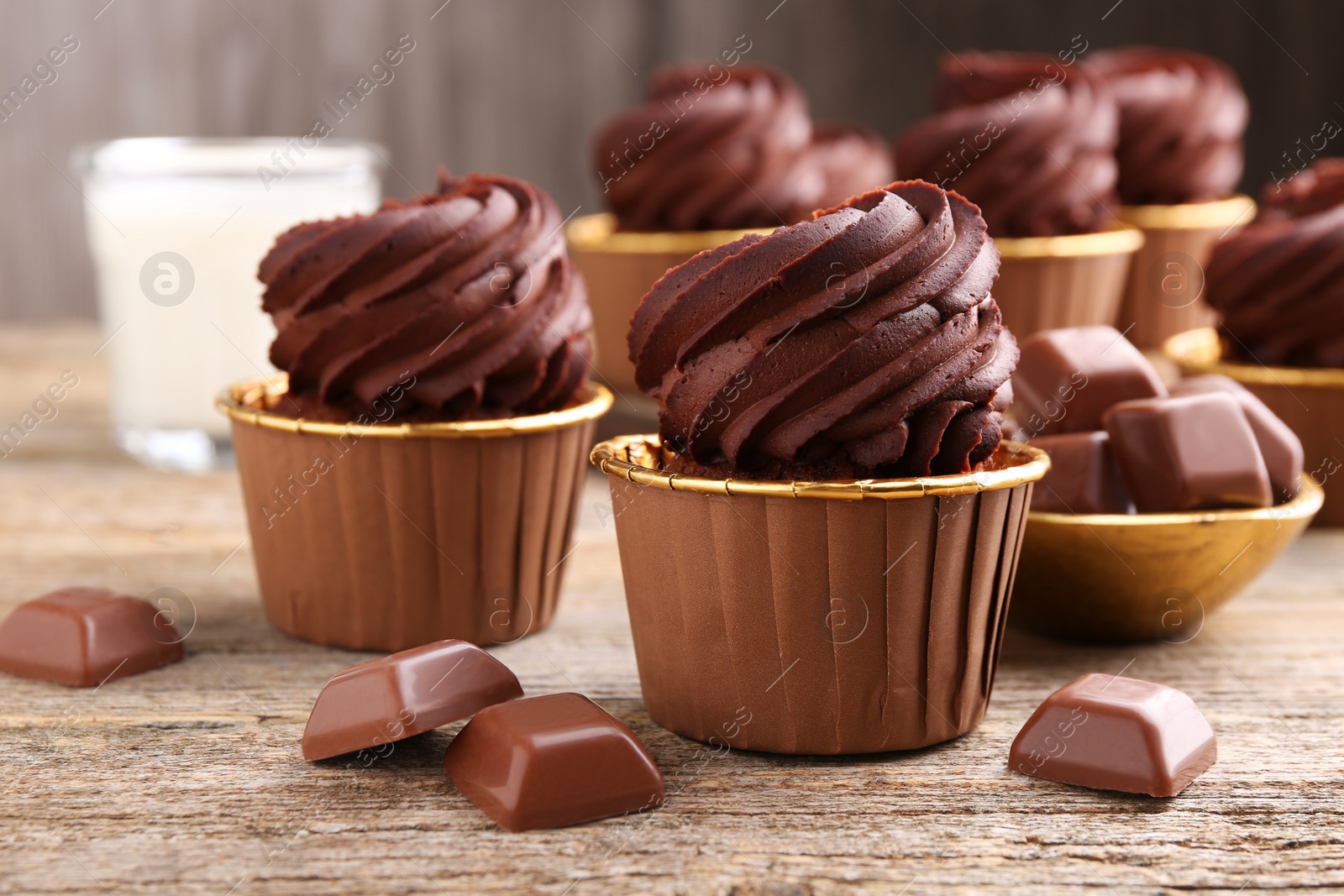 Photo of Delicious cupcakes and chocolate pieces on wooden table, closeup